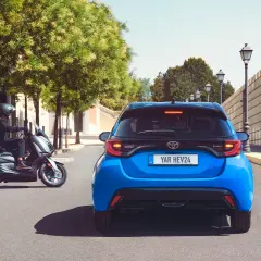 Niebieski Toyota Yaris HEV. Kierowca na skuterze obok. Szukasz "toyota yaris instrukcja obsługi po polsku"?