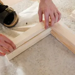 Ręce składają drewniane elementy, by stworzyć ramę ławki. To początek projektu jak zrobić ławkę DIY.