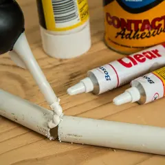 Aplikator nakłada klej na pękniętą rurkę, pokazując, jak skleić plastik z plastikiem. W tle tubki z klejem.