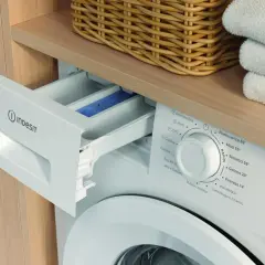 Szara szuflada na proszek w pralce Indesit, obok kosza z praniem. Instrukcja obsługi pomoże wybrać odpowiedni program.