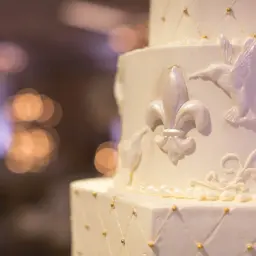 Biały tort weselny z ozdobami z masy cukrowej: lilie, kolibry i złote koraliki. Dowiedz się, jak przykleić ozdoby z masy cukrowej do tortu.