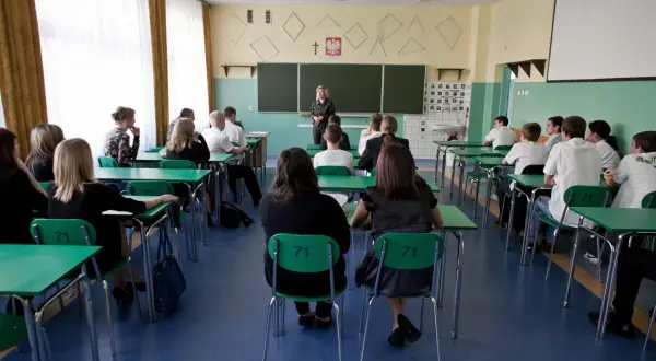 Lekcja w polskim gimnazjum, kiedy weszły gimnazja w polsce. Uczniowie siedzą w ławkach, nauczycielka stoi przy tablicy.