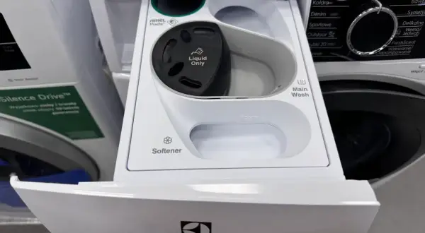 Szara przegródka na detergenty w pralce Electrolux ładowanej od góry. Widać miejsce na kapsułki Ariel, płyn do płukania i pranie główne.