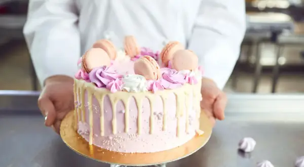 Różowy tort z makaronikami i kremem. Idealne ozdoby do tortu znajdziesz w cukierni.