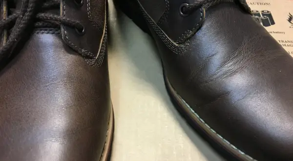 Brązowe, skórzane buty z ciemnymi sznurówkami. Skóra na jednym bucie jest lekko pognieciona, co może sugerować potrzebę dowiedzenia się, jak wyprostować skórę na butach.