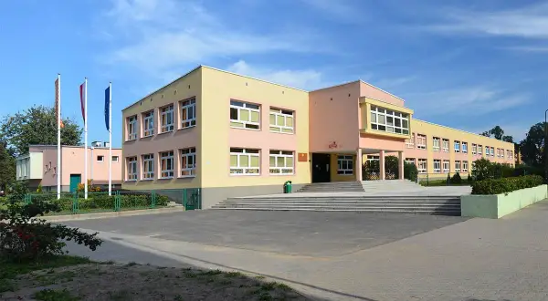 Kolorowy budynek szkoły z flagami przed wejściem. To miejsce, gdzie kiedy powstalo gimnazjum, uczniowie zdobywali wiedzę.