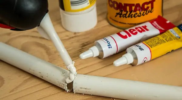 Aplikator nakłada klej na pękniętą rurkę, pokazując, jak skleić plastik z plastikiem. W tle tubki z klejem.