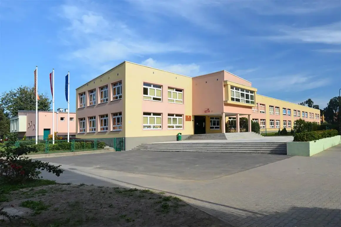 Kolorowy budynek szkoły z flagami przed wejściem. To miejsce, gdzie kiedy powstalo gimnazjum, uczniowie zdobywali wiedzę.