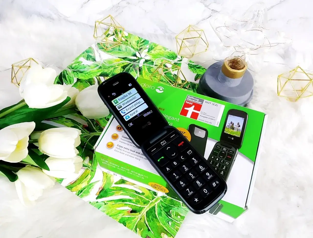 Otwarty telefon z klapką, na ekranie menu, obok pudełko z napisem