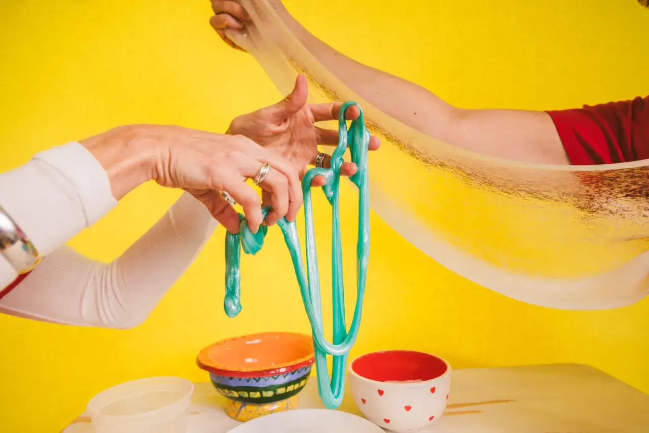 Ręce formują błyszczący, turkusowy slime, pokazując jak zrobić slime instrukcja krok po kroku.